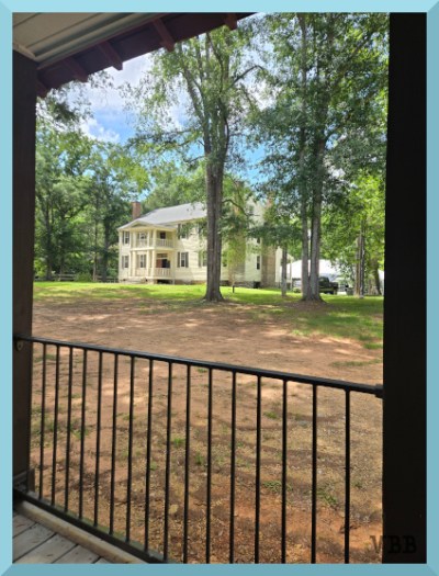 Photo of a yellow, two-story house, framed by porch roof and railings
