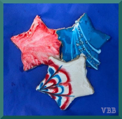 three star-shaped sugar cookies with red, white, and blue frosting on a blue background