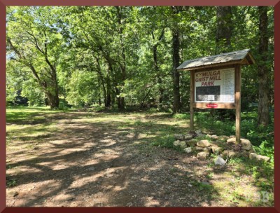 Photo of grass field, trees, and a trail head sign