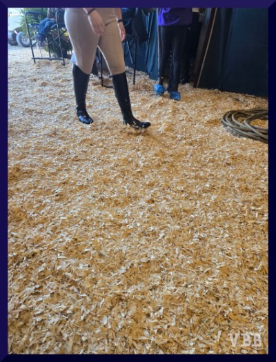 photo of a person in tall boots walking down an aisle filled with shavings