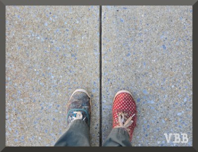 Photo of feet in mismatched sneakers standing on a concrete sidewalk