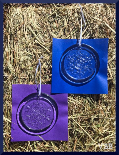 Photo of two glass snowflake ornaments on colored pieces of paper on a hay bale.