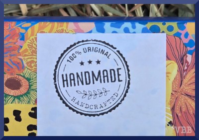 Photo of a label that says HANDMADE on part of a box sitting on a hay bale.