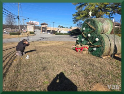 Photo of kneeling man taking picture of a tree made from rolls, with shadow of second photographer in foreground