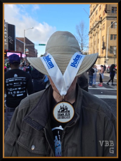Photo of person wearing a hat with medal draped over hat obscuring the face, on city street with people in background