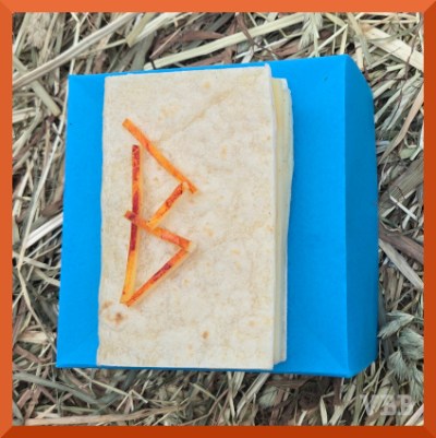 Edible book with the letter B on the cover, resting on a blue paper box resting on a hay bale.