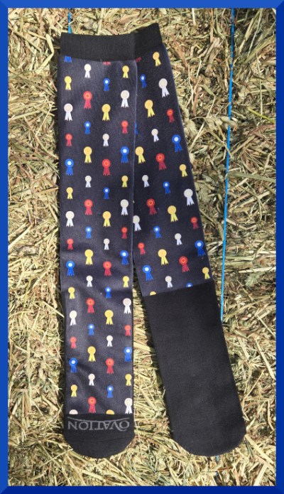 Photo of a pair of long socks decorated with horse show ribbons, lying on a hay bale