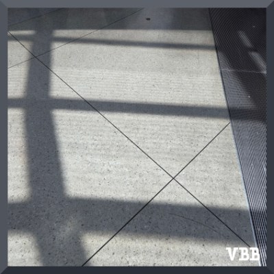 Photo of geometric shadows on a tiled floor, with grating on the right side