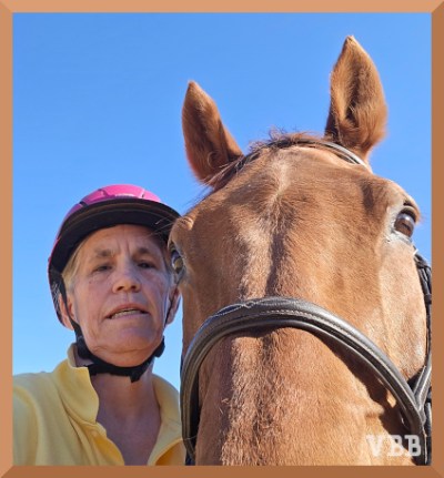 Selfie of a woman in a yellow shirt and pink helmet next to the face of a chestnut horse