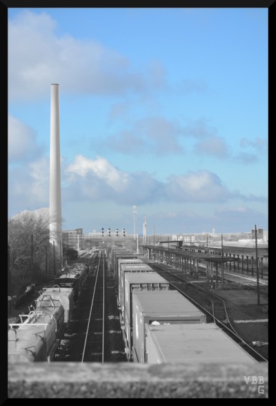Photo of black & white trains on tracks under blue sky with clouds.