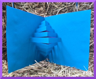 Photo of a blue paper card with a pop up strips and a purple paper backing