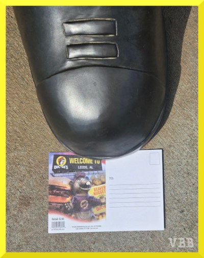 Photo of a postcard resting under the toe of a statue.