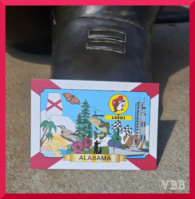 Photo of a postcard resting on the toe of a statue.