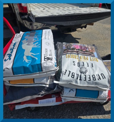 Photo of a pile of feed bags about to be loaded into the back of a pickup truck.