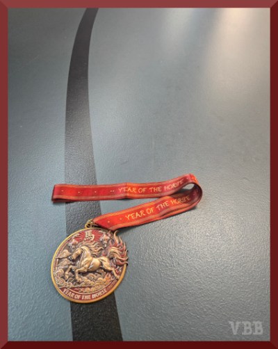 Photo of a red & gold medal with a red & gold ribbon lying on the black line of a track.