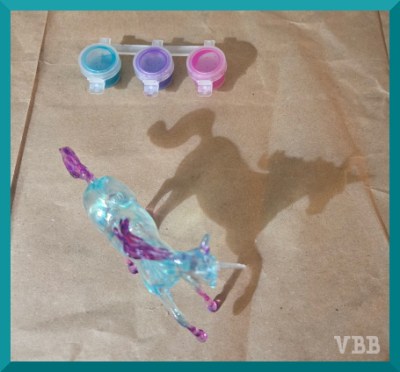 Photo of suncatcher model casting a shadow onto a brown paper surface, with paint pots in the background