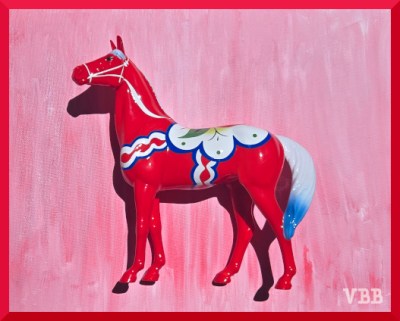 Photo of of red model horse with white and blue trim on a painted pink background.