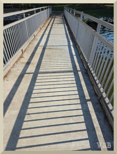 Photo of the bridge section of a fishing dock with railing shadow on the walkway.