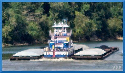 Blurry photo of a tug boat with barges on water with trees in the background.