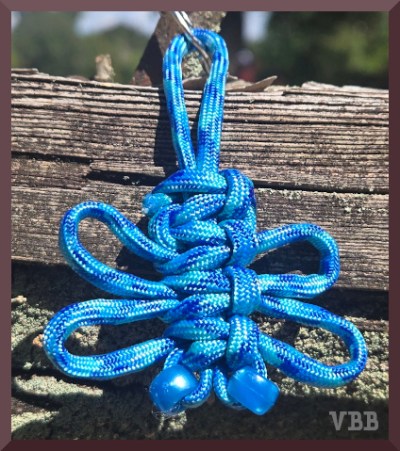 Close up photo of a blue macrame butterfly hanging on a section of wooden fencing.