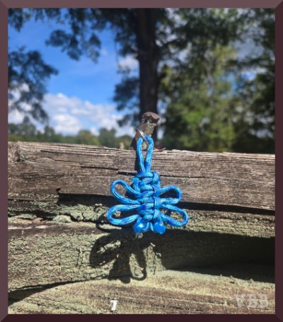 Photo of a blue macrame butterfly hanging on a section of wooden fencing.