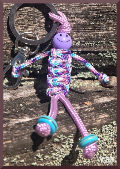 Close up photo of a pink macrame figure hanging on a section of wooden fencing.
