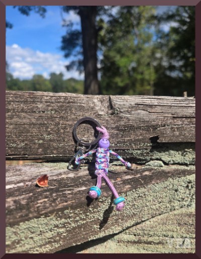 Photo of a pink macrame figure hanging on a section of wooden fencing.